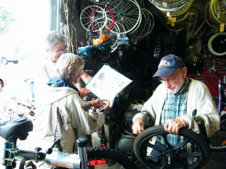 Rolly installing a new tire for Jean Beliveau. Jean is showing Rolly's wife Grace some pictures from his 11 year expedition.